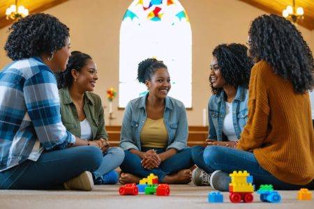 A diverse group of single mothers gathered in a church hall, participating in a supportive discussion with spiritual symbols in the background.